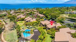 An aerial view of a resort with multiple bungalow-style buildings, a swimming pool, and a view of the ocean.