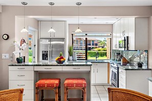 Een moderne keuken met een centraal eiland, roestvrijstalen apparatuur en uitzicht op een aangelegde tuin.