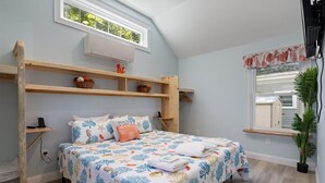 A bedroom with a bed, a window, a shelf, and a potted plant.