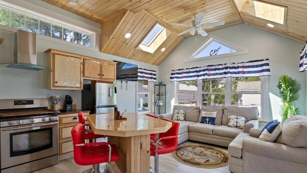 A modern kitchen with wooden cabinets, a central island with red bar stools, and a dining area.