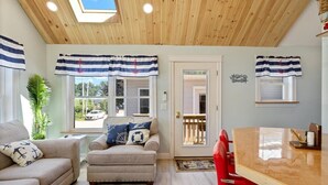 A cozy living room with a wooden ceiling, a dining table, and a red chair.