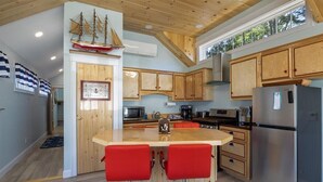 A modern kitchen with wooden cabinets, a central island with red bar stools, stainless steel appliances, and a ship model on the wall.