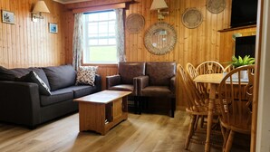 Un cuarto acogedor con piso de madera, un sofá, dos sillones, una pequeña mesa de madera y una mesa de comedor con sillas.