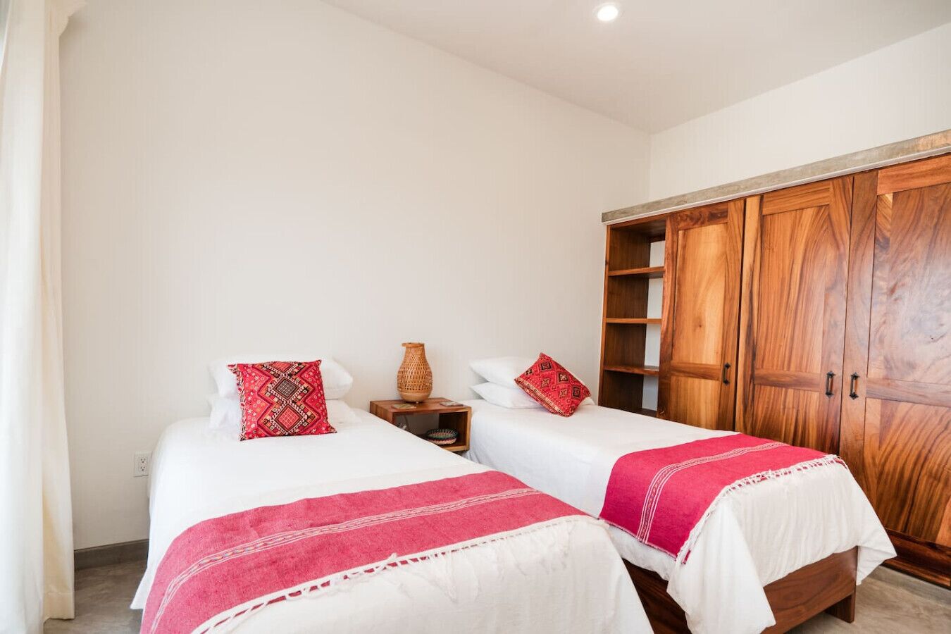 A room with two beds, a wooden wardrobe, and a small table with a vase.