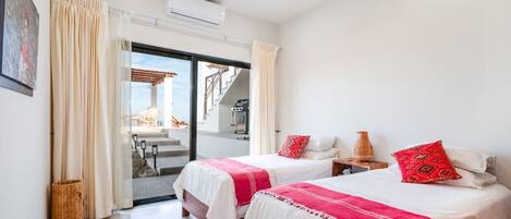 A hotel room with two beds, a ceiling fan, an air conditioning unit, and a view of the outside.