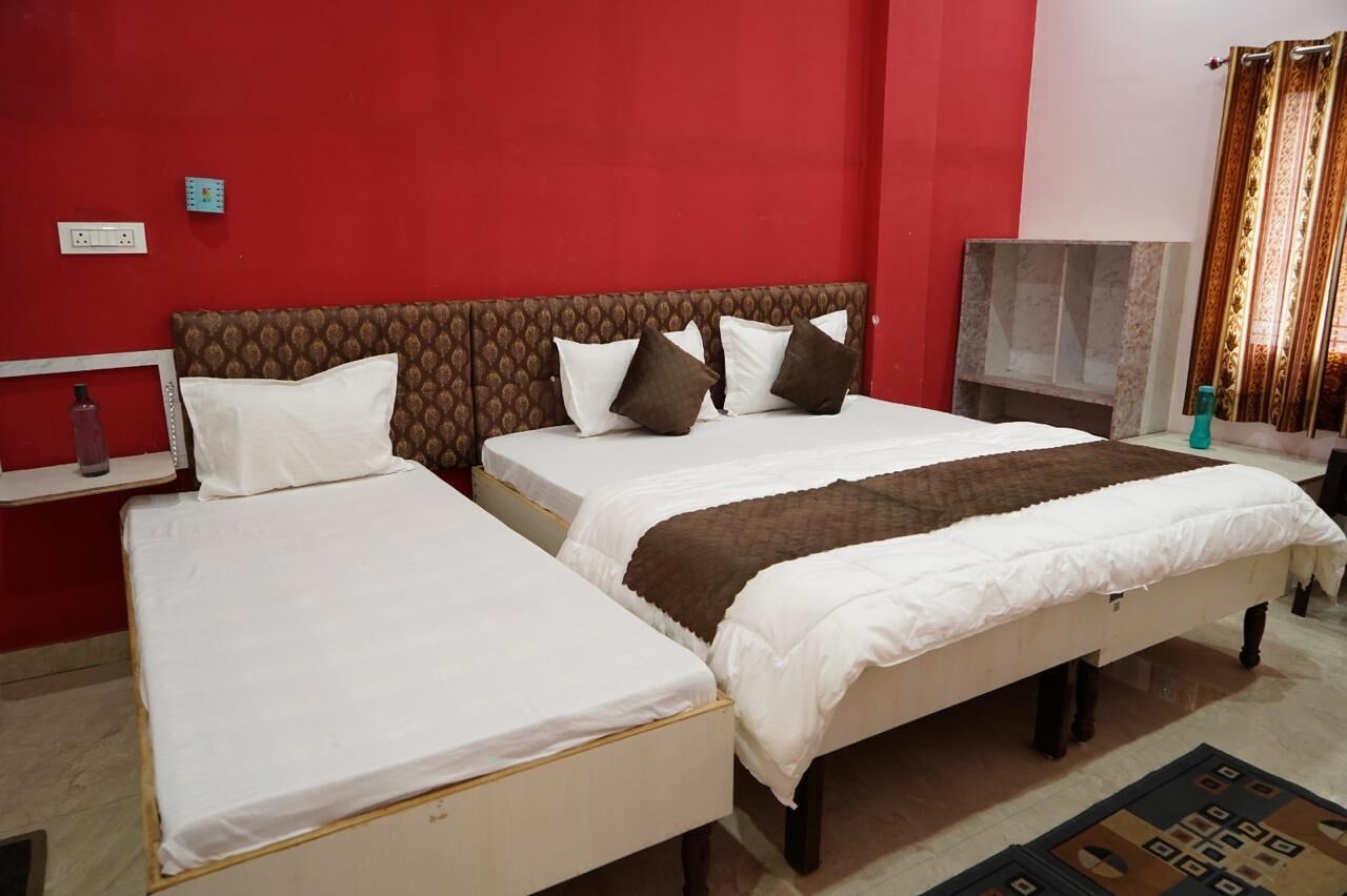 A hotel room with two single beds, a red accent wall, a brown headboard, and a small shelf with a bottle.