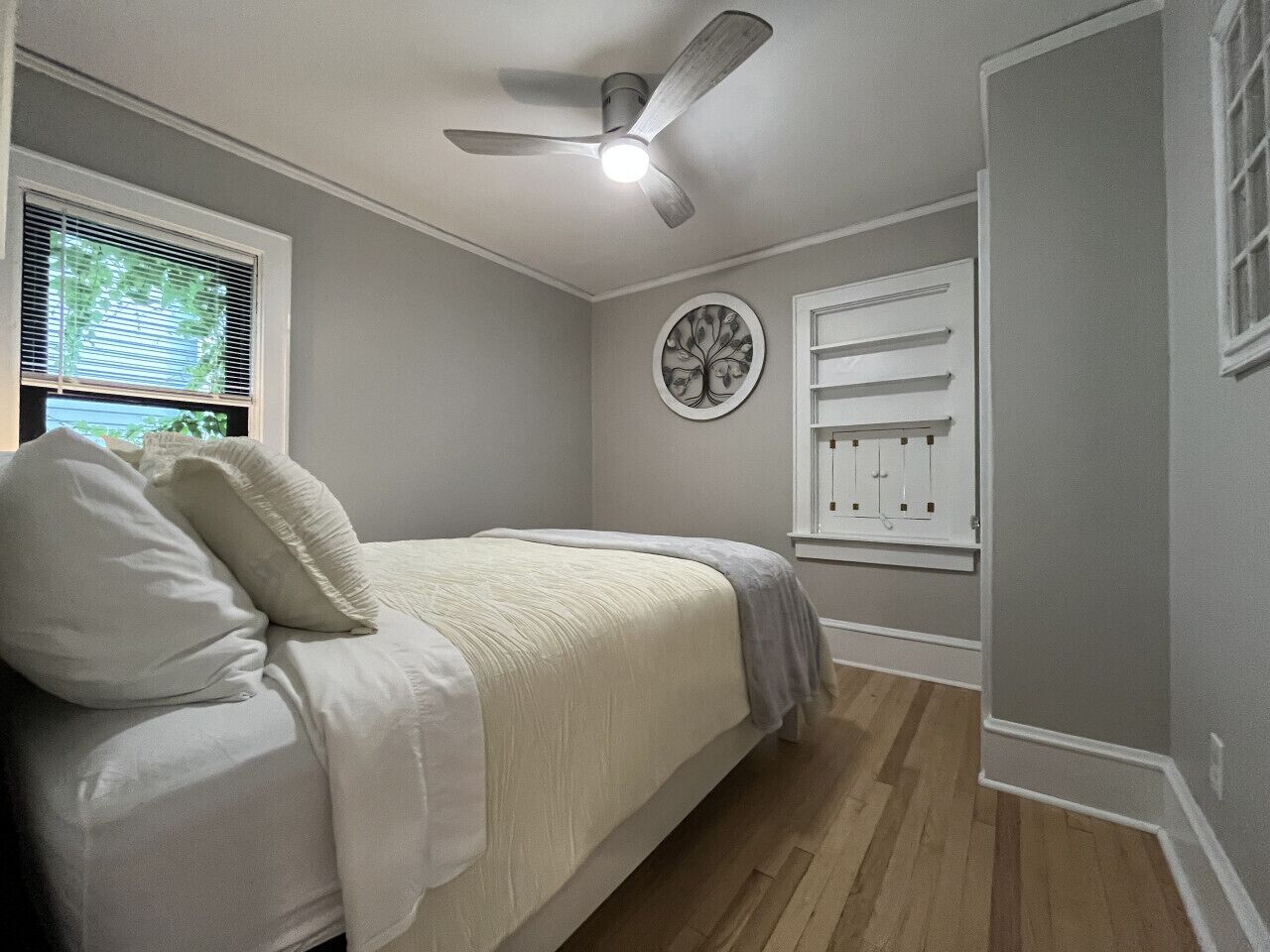 Een slaapkamer met een bed, een plafondventilator, een raam met zonwering, een wandlamp en een deur met een raampje.