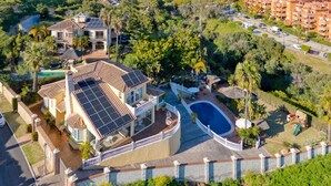An aerial view of a residential area with a large house featuring a swimming pool, solar panels, and a fenced garden. - Villa Oriente - Family Villa with pool in Marbella East (Marbella)