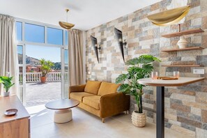 A living room with a sofa, a round coffee table, a potted plant, and a stone wall.