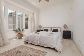 A bedroom with a large bed, two bedside tables, a potted plant, and a ceiling fan.