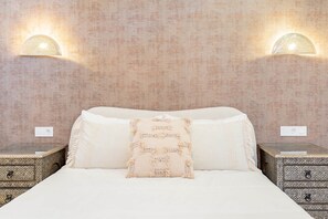 A bed with white linens, a beige throw pillow, and two nightstands with decorative patterns.