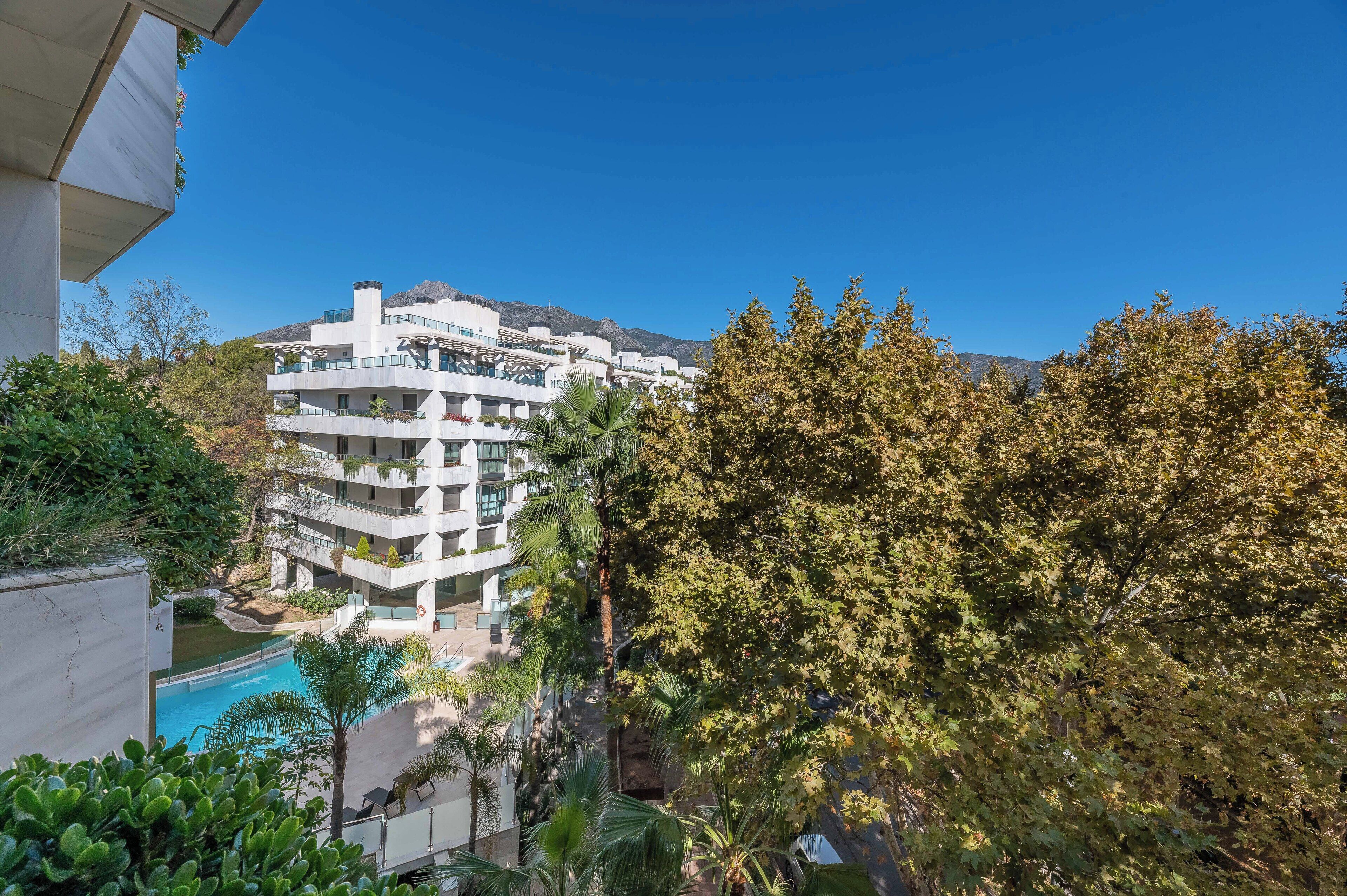 Un hotel de varios pisos con piscina, rodeado de árboles y montañas.