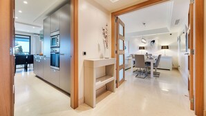 Une cuisine moderne dotée d’appareils électroménagers intégrés, un coin repas avec une table et des chaises blanches, et une console au design minimaliste.