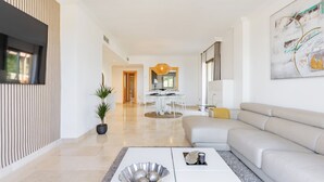 A modern living room with a sofa, a coffee table, and a dining area with a table and chairs. - Penthouse 2BR with Sea Views & Heated Pool (Benahavís)