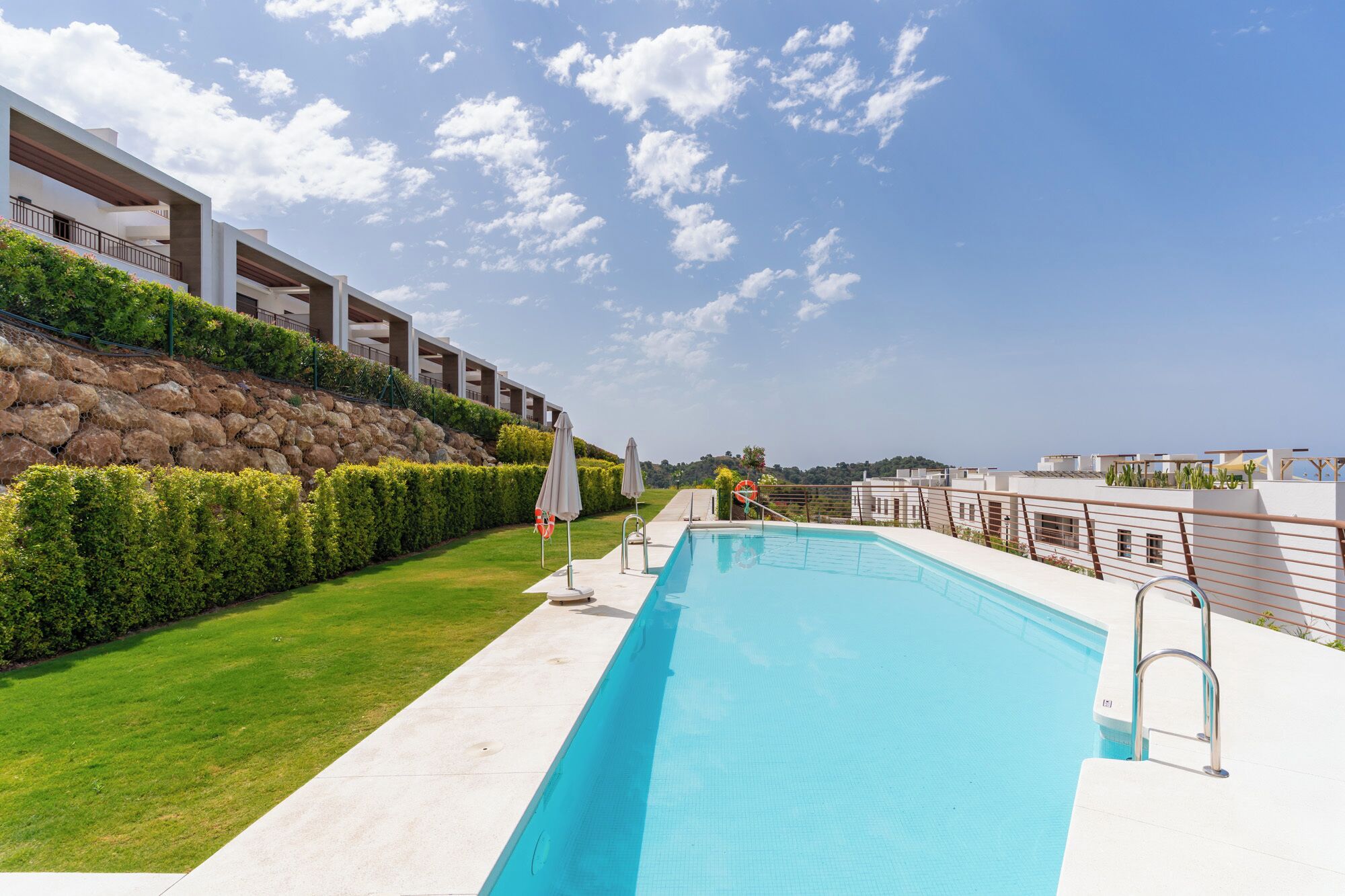 Una piscina d'aigua cristal·lina blava, envoltada per un solàrium blanc i una zona verda.