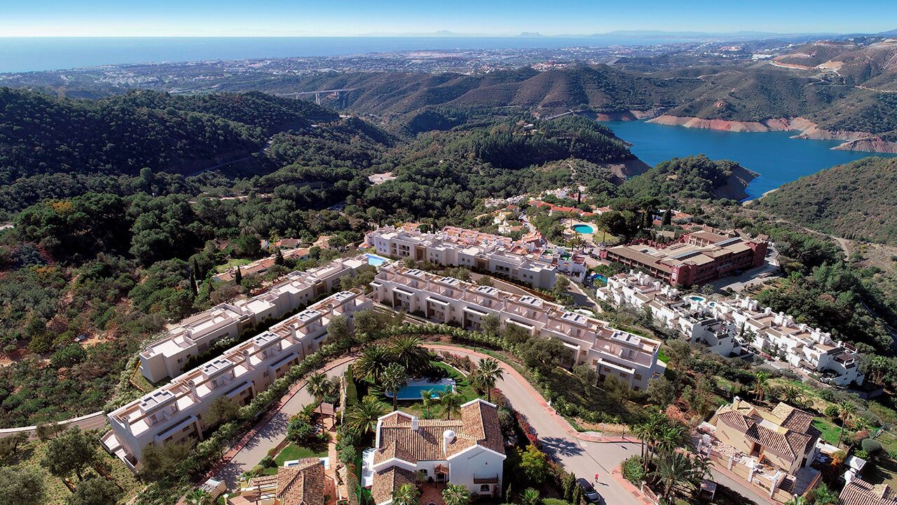 An aerial view of a resort with multiple buildings, a swimming pool, and a mountainous backdrop.