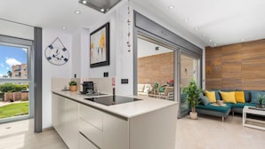 Eine moderne Küche mit einer zentralen Kochinsel, einem Essbereich mit einer Couch und einem Couchtisch, sowie eine große Schiebeglasdoor zum Patio.