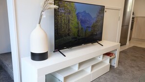 En platt-TV placerad på en vit TV-bänk med en hylla av glas under.