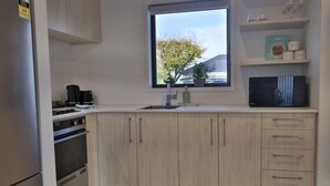 Ett modernt kök med ljusa träskåp, en inbyggd ugn, en kaffebryggare och ett fönster med utsikt över träd och ett hus.