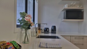 Une cuisine moderne avec un plan de travail blanc, un évier, une bouilloire et un vase rempli de fleurs.