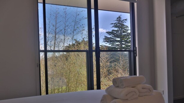 Une chambre d’hôtel avec une grande fenêtre, un lit recouvert de draps blancs et une pile de serviettes pliées.