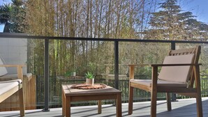 Une terrasse en bois avec une balustrade en verre, un fauteuil rembourré, une petite table agrémentée d’une plante, et une vue sur des arbres et une montagne.