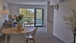 Un salon moderne avec une table ronde, des fauteuils gris, un canapé et un balcon offrant une vue sur les arbres.