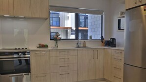 Une cuisine moderne dotée d’appareils électroménagers en acier inoxydable, de meubles en bois et d’une fenêtre offrant une vue sur le bâtiment extérieur.