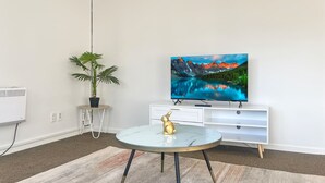 A modern living room with a flat-screen TV, a round table with a gold figurine, a potted plant, and a white entertainment unit.