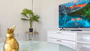 A modern living room with a glass coffee table, a white TV stand, a golden rabbit figurine, and a potted plant.