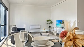 A modern living room with a dining area, a flat-screen TV, and a large window.