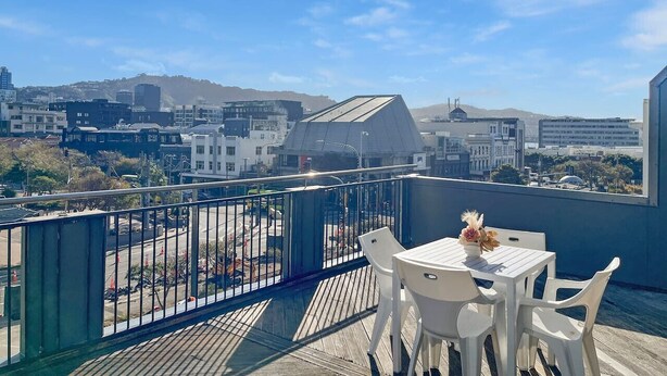 A rooftop terrace with a table and chairs, overlooking a cityscape with buildings and hills.