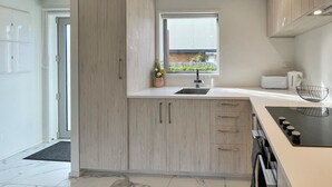 A modern kitchen with light wood cabinets, a white countertop, a built-in oven, and a window providing natural light. - Homey and Bright Riccarton 1BR (Christchurch)