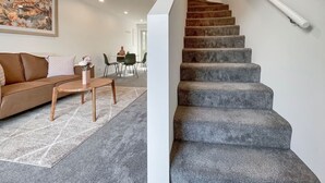 A staircase with a handrail, a living room with a sofa, a coffee table, and a painting on the wall. - Homey and Bright Riccarton 1BR (Christchurch)