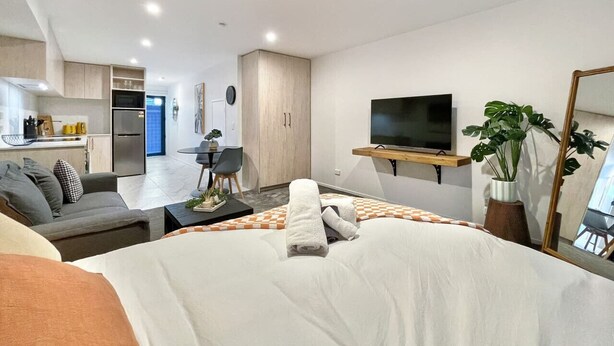 Une chambre d’hôtel moderne, dotée d’un grand lit, d’un canapé, d’une table à manger et d’un coin cuisine à l’arrière-plan.