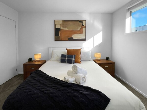 Una camera d'hotel con un letto grande, due comodini con lampade, un quadro appeso al muro e una finestra vista.