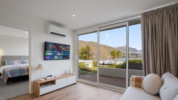 Une chambre d’hôtel moderne dotée d’un grand lit, d’un téléviseur fixé au mur, d’un canapé et d’une porte-fenêtre coulissante donnant sur un balcon avec une vue panoramique.