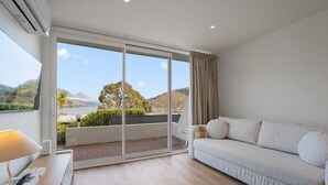 Une chambre moderne avec un canapé, une lampe et une vue sur un paysage naturel, visible à travers de grandes portes vitrées.