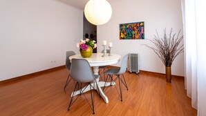 A dining area with a round table, grey chairs, a vase with flowers, a hanging light, and a radiator.