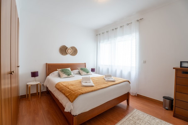 Ein Schlafzimmer mit einem hölzernen Bett, einem Nachttisch, einer Lampe, einem Mülleimer und einem Kleiderschrank.