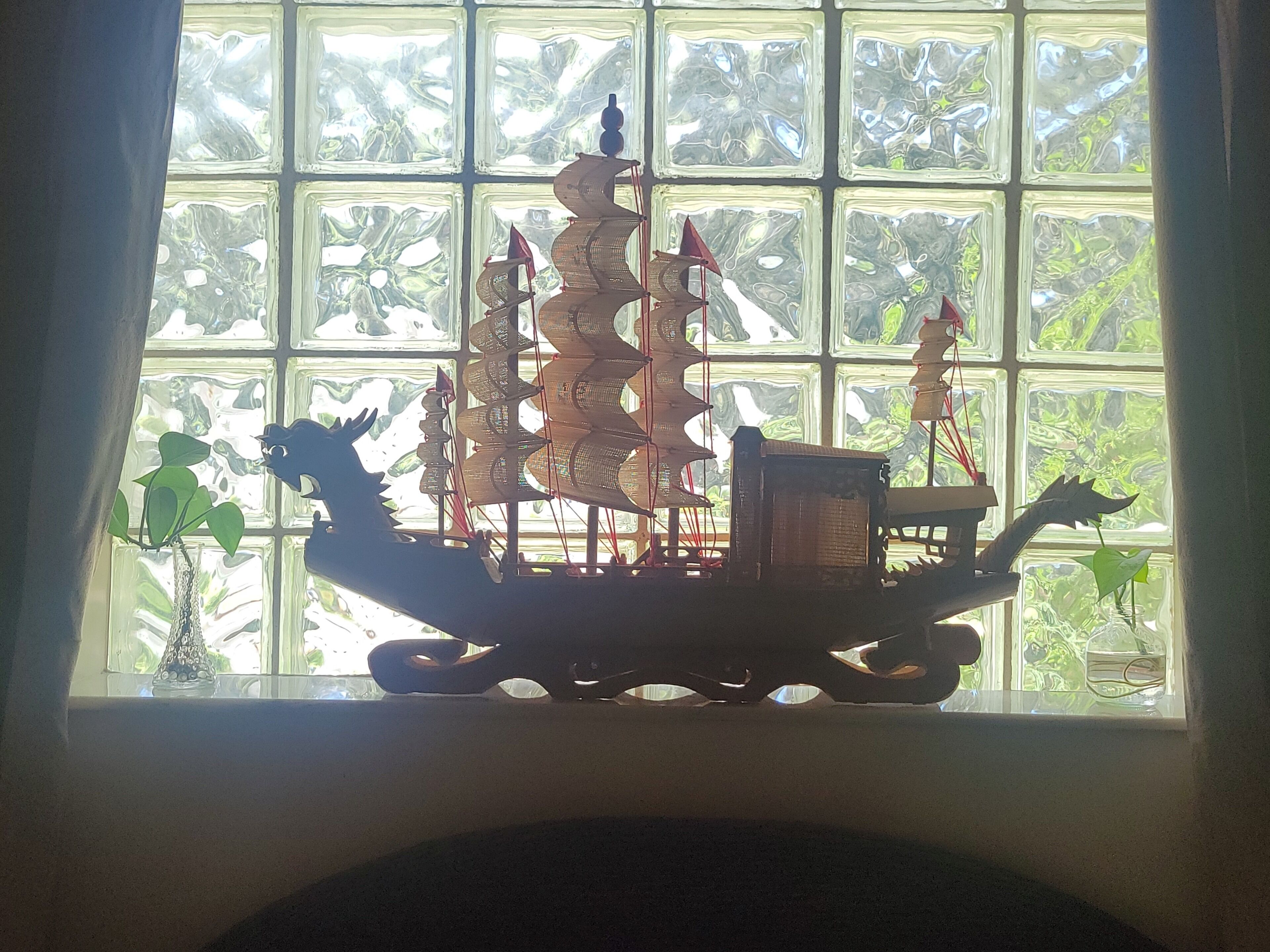 A model ship in a window with a view of greenery outside.