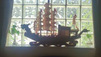 A model ship in a window with a view of greenery outside.