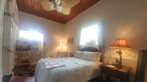 A bedroom with a bed, bedside lamps, a ceiling fan, a window, and a TV.