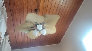 A ceiling fan with five blades and a light fixture in a room with wooden paneling.