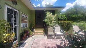 A green house with a covered patio, potted plants, and outdoor furniture.