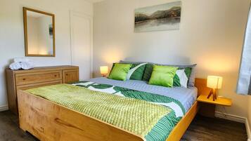 Une chambre à coucher avec un lit en bois, une literie verte et blanche, une lampe de chevet, un miroir et un tableau accroché au mur.