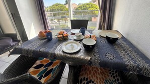 A balcony table set with breakfast items, a wicker chair, and a view of the city.