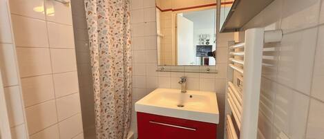 A bathroom with a white sink, red cabinet, and a shower curtain.