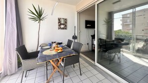 A dining area with a table set for two, a television mounted on the wall, and a sliding glass door leading to an outdoor balcony.