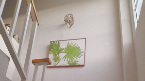 Uma escada com corrimão, um candeeiro fixado na parede e uma impressão botânica emoldurada.